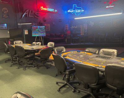 Poker tables set up in a dimly lit gaming room with a neon signs.